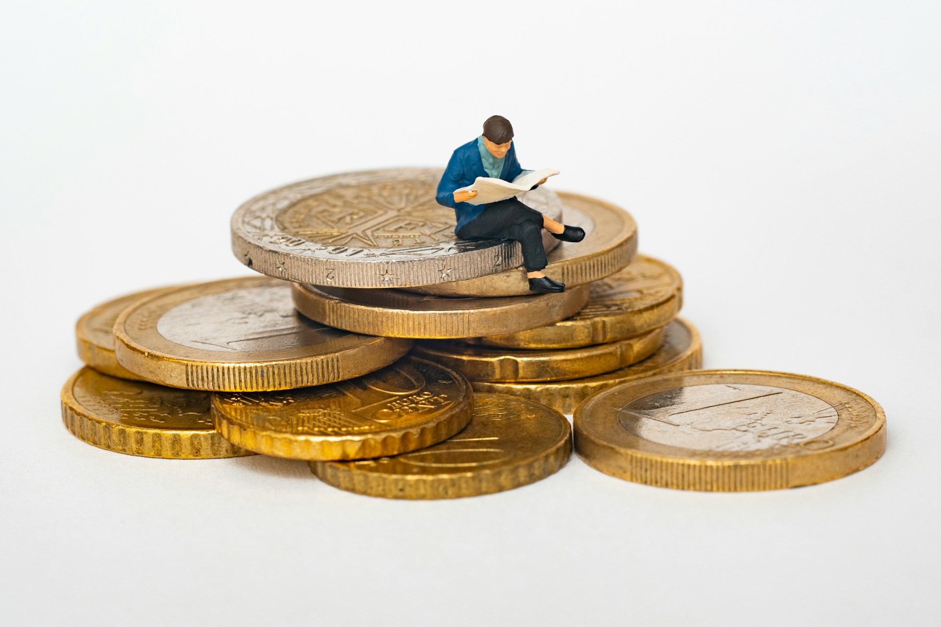 a small man reading on top of Euro coins