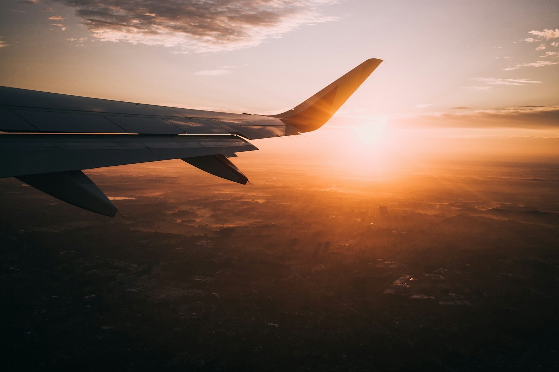 an airplane wing with the sun on the horizon